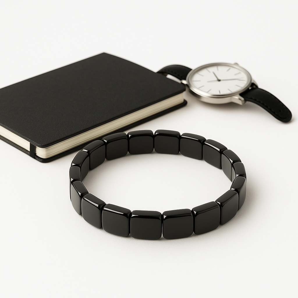 Bracelet hématite noir pour homme posé avec une montre en cuir sur fond blanc — bijou masculin élégant et énergétique.