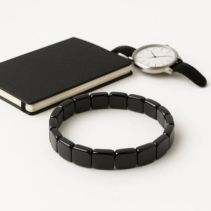 Bracelet hématite noir pour homme posé avec une montre en cuir sur fond blanc — bijou masculin élégant et énergétique.